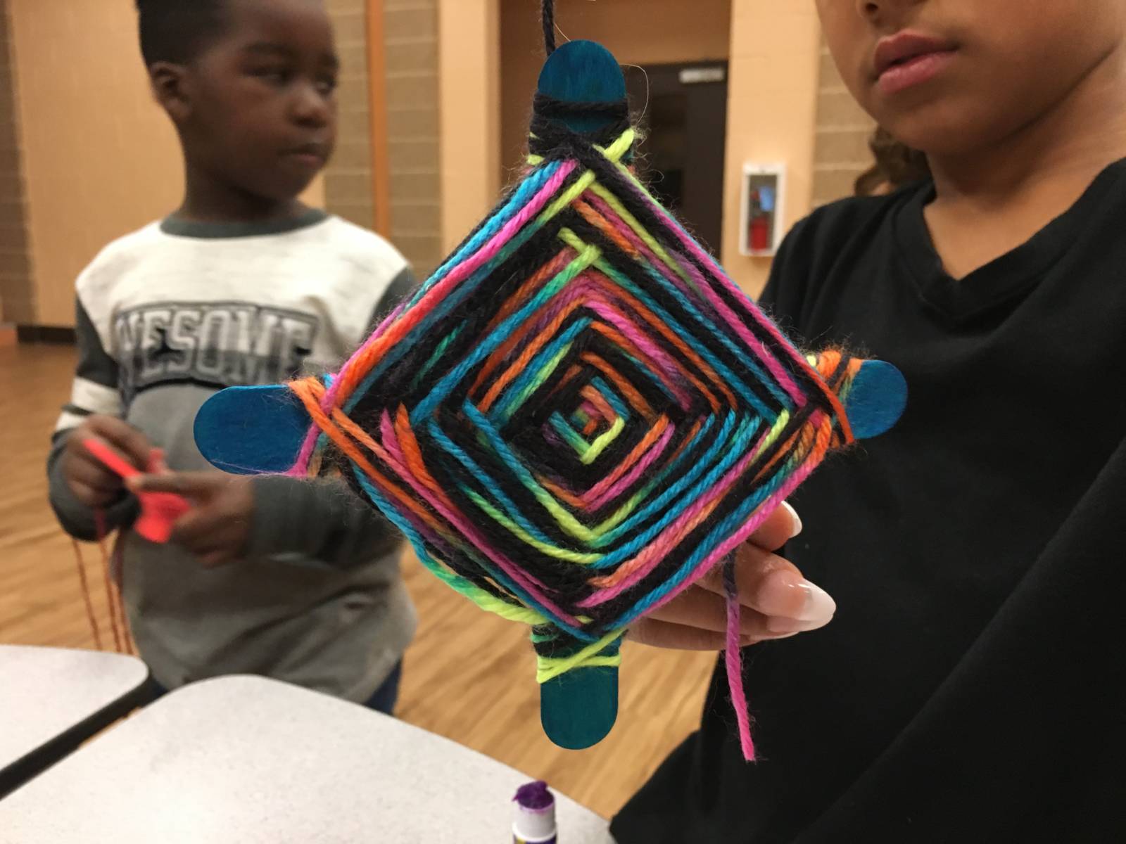 Kid holding up art project made of sticks and yarn